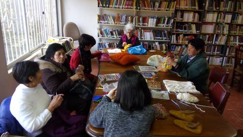 Un grupo de mujeres se reúne en una biblioteca para participar en una actividad de tejido y manualidades.