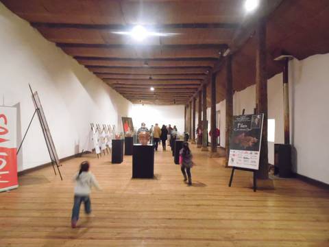 Una sala de exposición con varias personas y niños corriendo en el interior.