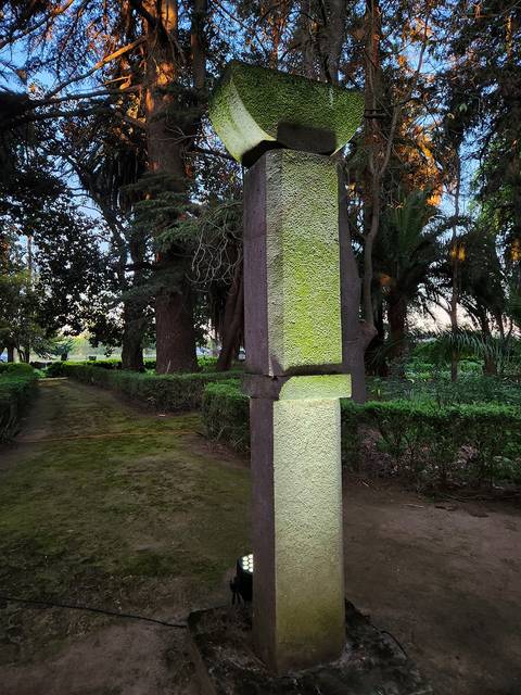 Una escultura moderna se eleva en un jardín rodeado de árboles y vegetación.