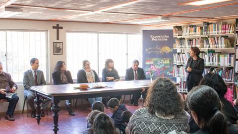 Una charla en una biblioteca donde se presentan diversas personas sentadas frente a un expositor que está hablando.
