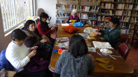 Un grupo de mujeres está participando en una actividad de manualidades en un espacio con estanterías de libros.