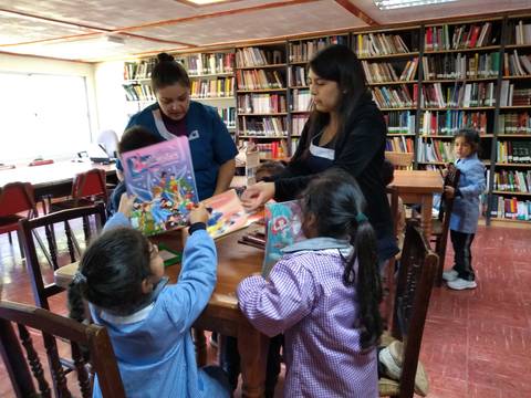 Un grupo de niños y adultos interactúan en una biblioteca, mostrando libros y manualidades.