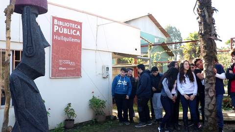 Un grupo de personas se encuentra frente a la Biblioteca Pública de Huilquilemu, con una escultura grande de fondo.