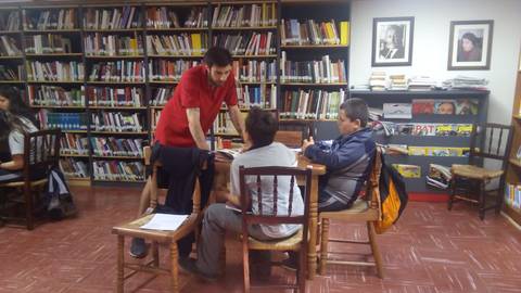 Un grupo de personas estudiando en una biblioteca con estanterías llenas de libros.