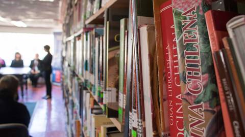 Una vista de una biblioteca con estanterías llenas de libros y personas al fondo en un evento.