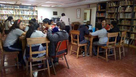 Un grupo de estudiantes está trabajando en mesas dentro de una biblioteca.