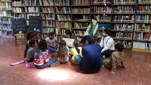 Un grupo de niños escucha atentamente mientras se realiza una actividad en una biblioteca.