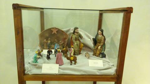 Una vitrina exhibe un belén con figuras artesanales de la Sagrada Familia y otros personajes.