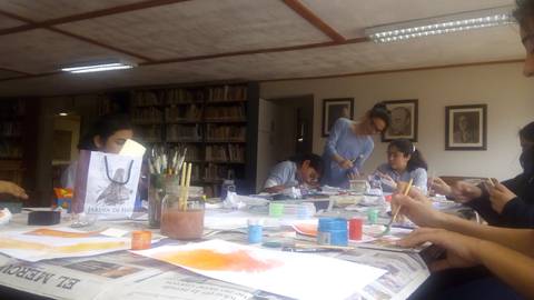 Un grupo de niños y adultos están creando arte en una mesa llena de materiales en un entorno de biblioteca.