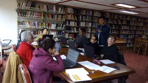 Un grupo de personas se encuentra en una sala de estudio, trabajando en computadoras portátiles dentro de una biblioteca.
