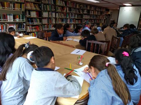 Un grupo de niños trabajando en una biblioteca, dibujando y tomando apuntes.