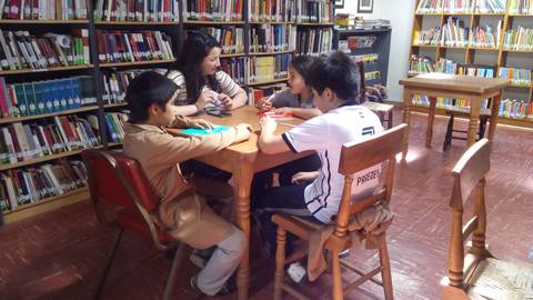 Cuatro niños y una mujer están sentados alrededor de una mesa en una biblioteca.