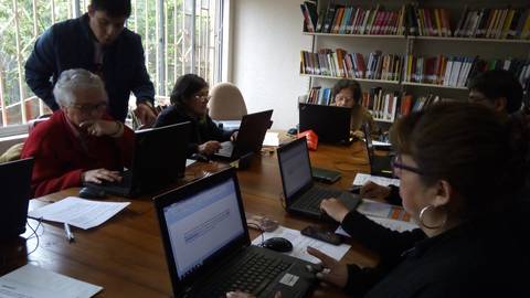 Un grupo de personas mayores se encuentra en una sala utilizando computadoras portátiles mientras participan en una actividad de aprendizaje.