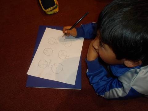 Un niño dibuja en una hoja de papel mientras se apoya en su mano.