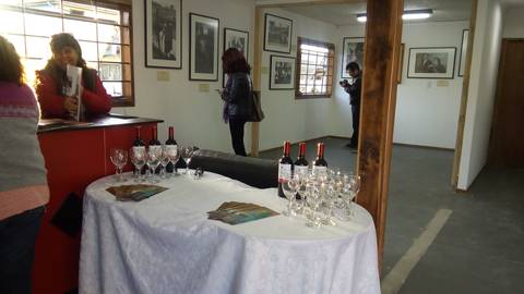 Una sala de exposición con fotografías en las paredes y una mesa con copas y botellas de vino.