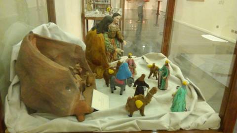 Una escena de un nacimiento con figuras de madera y personajes de colores en un vitrina.