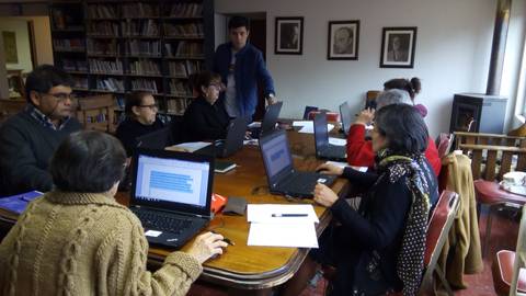 Un grupo de personas trabaja en sus computadoras portátiles alrededor de una mesa en una sala de estudio.