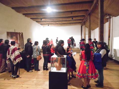 La imagen muestra a un grupo de personas en una sala de museo, algunas vestidas con trajes tradicionales, interactuando y observando una exhibición.