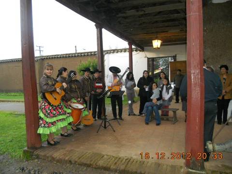 Un grupo de músicos vestidos con trajes tradicionales interpreta música en un ambiente festivo frente a un porche.