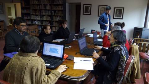 Un grupo de personas asistiendo a una clase de informática en una sala con computadoras portátiles.