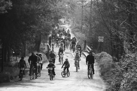 Un grupo de personas montando en bicicleta por un camino rural en blanco y negro.