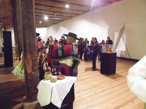 Un grupo de personas en un evento cultural, con vestimentas tradicionales y una exposición de arte detrás.