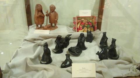 La imagen muestra una vitrina con figuras de cerámica, incluyendo dos estatuillas de personas y varios objetos negros que parecen ser artesanías.