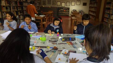 Un grupo de niños y niñas están realizando manualidades en una biblioteca.
