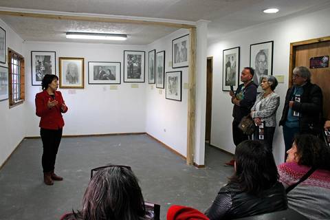 Una mujer habla frente a un grupo de personas en una sala de exposición llena de fotografías enmarcadas.