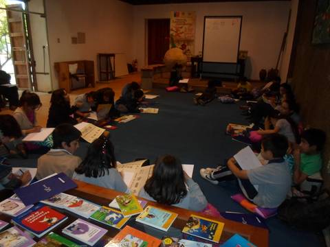 Un grupo de niños sentados en el suelo, dibujando y escribiendo con libros y materiales alrededor.