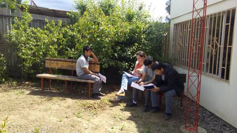 Un grupo de cuatro personas sentadas en un banco al aire libre, revisando documentos en un ambiente natural.