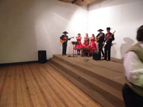 Un grupo de músicos y bailarinas vestidas de rojo se presentan en un escenario con un ambiente festivo.