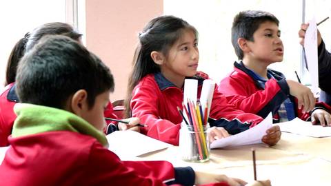 Un grupo de niños en un aula escucha y participa activamente en una actividad académica.