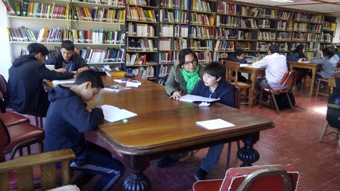 Un grupo de estudiantes trabaja en una biblioteca con estanterías llenas de libros.