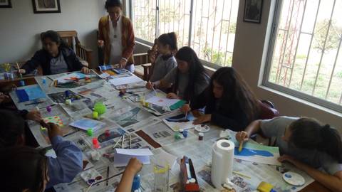 Un grupo de jóvenes está pintando y creando artísticamente en un taller rodeado de materiales y obras en progreso.