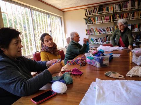 Un grupo de mujeres se reúne en una sala para tejer y compartir, rodeadas de lanas y materiales diversos.