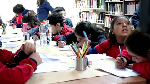 Un grupo de niños trabajando en una actividad escolar en un aula con estanterías de libros al fondo.