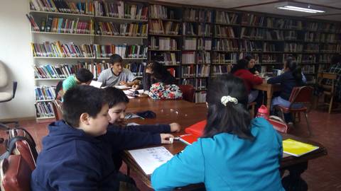 Un grupo de niños estudia y realiza actividades en una biblioteca.