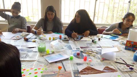 Grupo de jóvenes pintando en una mesa llena de materiales artísticos.