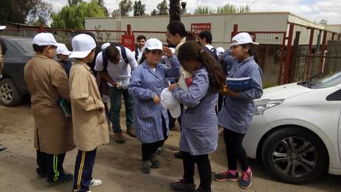 Un grupo de niños en un entorno exterior, vestidos con delantales y gorras, interactuando entre ellos.