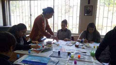 Un grupo de estudiantes participan en una clase de arte en la que utilizan pinturas y materiales creativos.