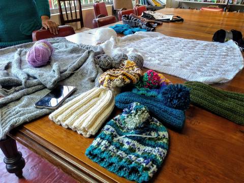 La imagen muestra varios gorros de lana y ovillos de hilo sobre una mesa de madera.