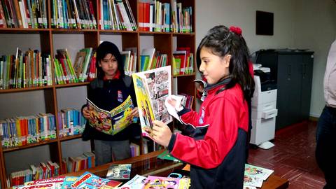Dos niños están en una biblioteca mirando cómics y libros.