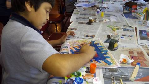 Un niño pinta en una mesa cubierta de periódicos y materiales de arte.