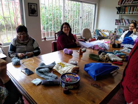 Un grupo de personas se reúne en una mesa para tejer y compartir momentos en un ambiente acogedor.