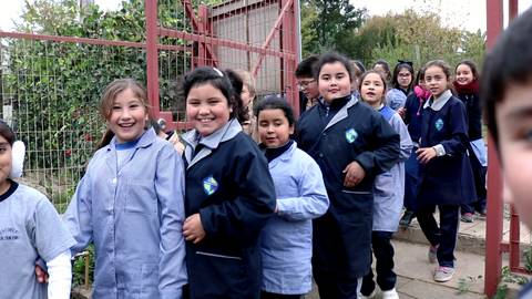 Un grupo de niñas sonrientes camina hacia la cámara en un ambiente escolar.