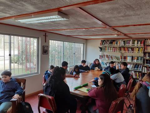 Un grupo de estudiantes reunidos en una biblioteca alrededor de una mesa de estudio.