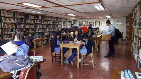 Una biblioteca con estudiantes leyendo y estudiando en mesas de trabajo.