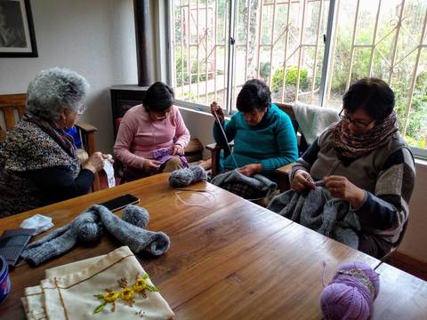 Un grupo de mujeres sentadas en una mesa, trabajando en sus proyectos de tejido en un ambiente acogedor.