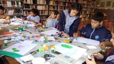 Un grupo de niños crea manualidades en una mesa llena de materiales artísticos en una biblioteca.